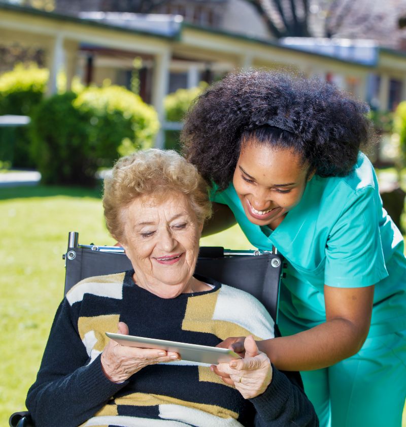 Caregivers at home Disabled elderly lady showing photos of her grandchildren on tablet to caregiver